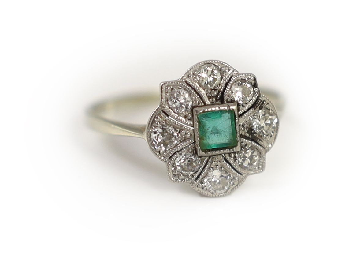 A 1920's white gold, millegrain set emerald and diamond cluster ring